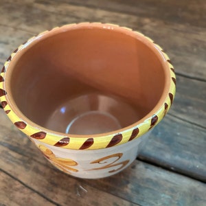 May include: A terracotta pot with a yellow and brown striped rim and a white base with a brown floral design.