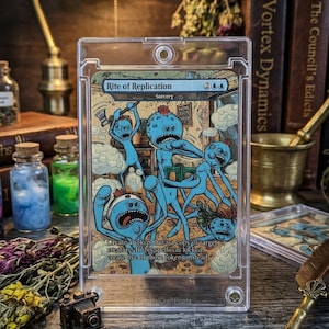 K&ouml;nnte beinhalten: Eine Sammelkarte mit blauen Cartoon-Charakteren mit roten Haaren und w&uuml;tenden Ausdr&uuml;cken. Die Karte tr&auml;gt den Titel "Rite of Replication" und enth&auml;lt den Text "Create a token that's a copy of target creature." Die Karte befindet sich in einer Schutzh&uuml;lle.