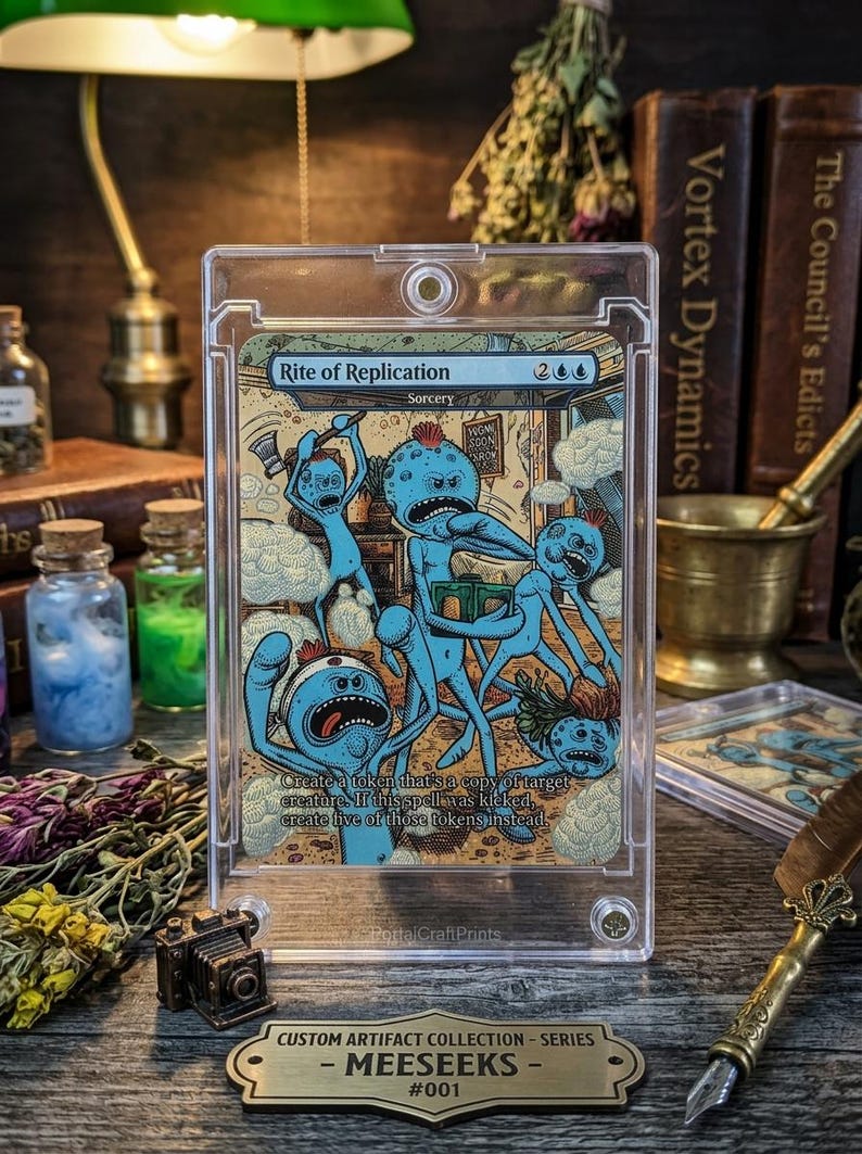 K&ouml;nnte beinhalten: Eine Sammelkarte mit blauen Cartoon-Charakteren mit roten Haaren und w&uuml;tenden Ausdr&uuml;cken. Die Karte tr&auml;gt den Titel "Rite of Replication" und enth&auml;lt den Text "Create a token that's a copy of target creature." Die Karte befindet sich in einer Schutzh&uuml;lle.