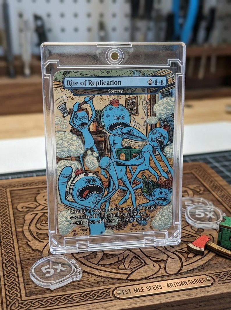 K&ouml;nnte beinhalten: Ein klarer Kunststoffkartenhalter mit einer Magic: The Gathering-Karte. Die Karte zeigt eine Cartoon-Illustration von blauen Kreaturen. Die Karte ist mit "Rite of Replication" und "Sorcery" beschriftet. Der Halter liegt auf einer Holzoberfl&auml;che mit ge&auml;tzten Designs und Acryl-Tokens.
