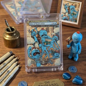 K&ouml;nnte beinhalten: Eine "Rite of Replication"-Karte in einer durchsichtigen H&uuml;lle mit blauen Cartoon-Charakteren. Eine kleine Holzfigur eines blauen Charakters mit einem Hammer befindet sich neben der Karte. Weitere Artikel sind Stifte, Token und ein gerahmter Druck.