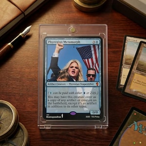 May include: A Magic: The Gathering card, "Phyrexian Metamorph," in a protective case. The card features an image of a woman raising her fist with an American flag in the background. Other cards and a compass are visible.