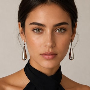 May include: A pair of polished silver-tone drop earrings featuring a smooth, elongated teardrop shape suspended from a simple vertical bar attachment. The earrings have a reflective, metallic finish and a clean, minimalist design structure.