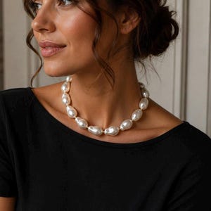 May include: A pearl necklace featuring large, irregularly shaped, off-white pearls. The pearls are strung together with a delicate gold-colored chain. The necklace is a statement piece, suitable for special occasions or adding elegance to any outfit.