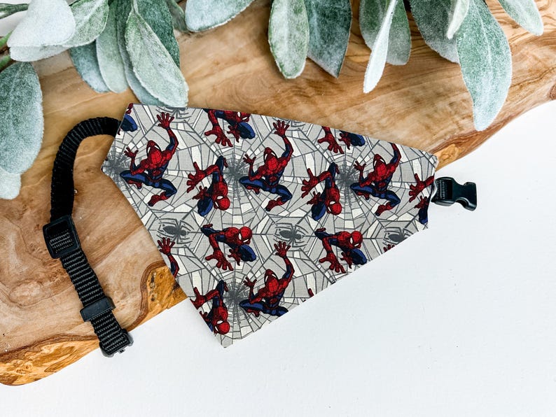 A Spiderman-themed bandana is displayed on a wooden surface, with a black leash attached to it.