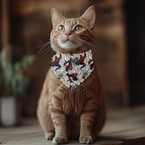 A ginger cat wearing a Spiderman-themed bandana sits on a wooden surface, looking up with a curious expression.