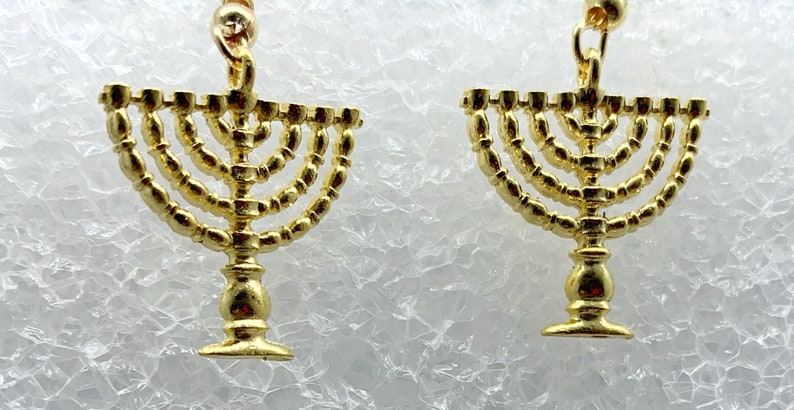 May include: A pair of gold-tone earrings featuring a menorah design. The menorah is a traditional Jewish symbol of the Festival of Lights, Hanukkah.