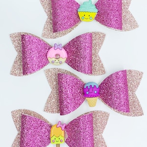 May include: Four pink glitter hair bows with different colorful food-themed buttons. The buttons are a cupcake, a donut, an ice cream cone, and a popsicle.