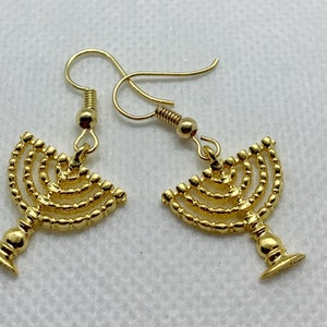May include: A pair of gold-toned earrings featuring a menorah design. The earrings are made of metal and have a dangling style.