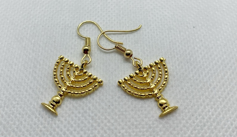 May include: A pair of gold-toned earrings featuring a menorah design. The earrings are made of metal and have a dangling style.