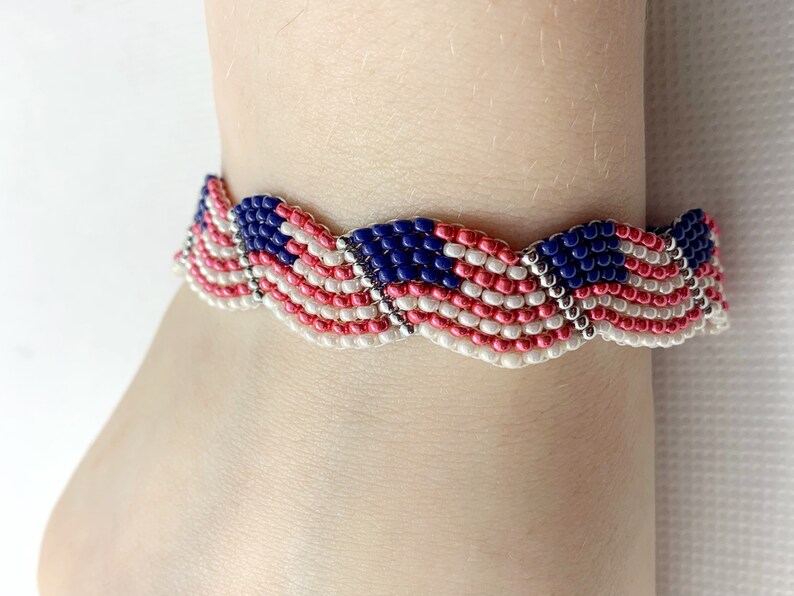 May include: A beaded bracelet featuring a design reminiscent of the American flag. The bracelet showcases alternating stripes of red and white beads, with a section of blue beads representing the stars. The bracelet is worn on a wrist.