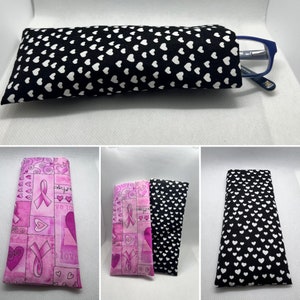 May include: Three eyeglass cases. One is black with white hearts, one is pink with a ribbon and hearts, and one is pink with a ribbon and a swirl pattern.