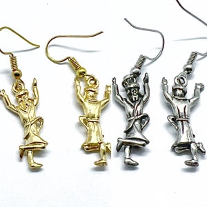 May include: A pair of gold and silver earrings featuring a small figurine of a person with arms raised in the air. The earrings are on a white background.