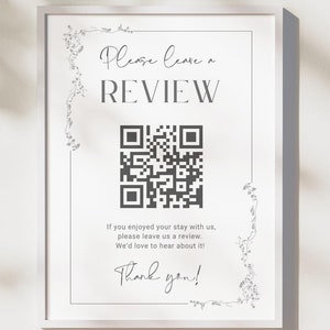 May include: A white sign with a black border and floral accents. The sign says "Please leave a REVIEW" and has a QR code. The text below the QR code says "If you enjoyed your stay with us, please leave us a review. We'd love to hear about it! Thank you!"