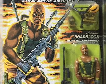 May include: A vintage action figure of Roadblock from the G.I. Joe toy line. The figure is wearing a green and brown camouflage uniform and holding a large machine gun. The figure is packaged in a plastic blister pack with a colorful cardboard backing. The packaging features the G.I. Joe logo and the words "A Real American Hero".