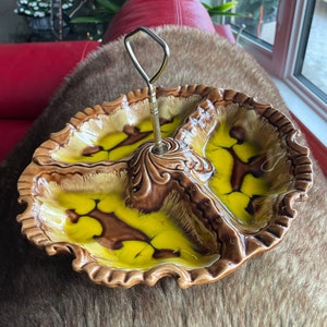 Könnte beinhalten: Eine braune und gelbe Keramik-Servierplatte mit drei Abschnitten und einem Metallgriff. Die Platte hat ein Wirbelmuster und einen gewellten Rand.