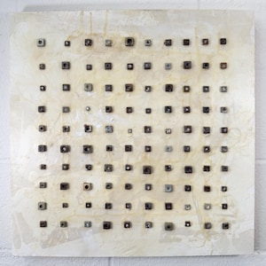 May include: Abstract artwork featuring a square canvas with a textured, off-white background. Numerous small, square, dark-colored objects are evenly spaced across the surface, creating a grid-like pattern. The artwork has a minimalist aesthetic.