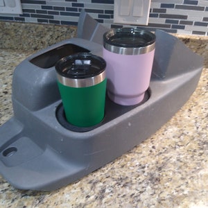 May include: A gray plastic cup holder with two stainless steel travel mugs. One mug is green and the other is purple.