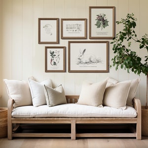 K&ouml;nnte beinhalten: Ein wei&szlig;es Leinen-Sofa mit drei Kissen steht vor einer wei&szlig;en Wand mit f&uuml;nf gerahmten botanischen Drucken. Eine Topfpflanze steht in der Ecke des Raumes.