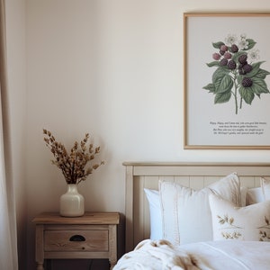K&ouml;nnte beinhalten: Ein gerahmter botanischer Druck eines Brombeerstrauchs mit gr&uuml;nen Bl&auml;ttern und violetten Beeren. Der Druck hat einen wei&szlig;en Hintergrund und einen hellen Holzrahmen. Der Druck h&auml;ngt an einer wei&szlig;en Wand &uuml;ber einem Bett mit wei&szlig;en Bettw&auml;sche und Kissen.