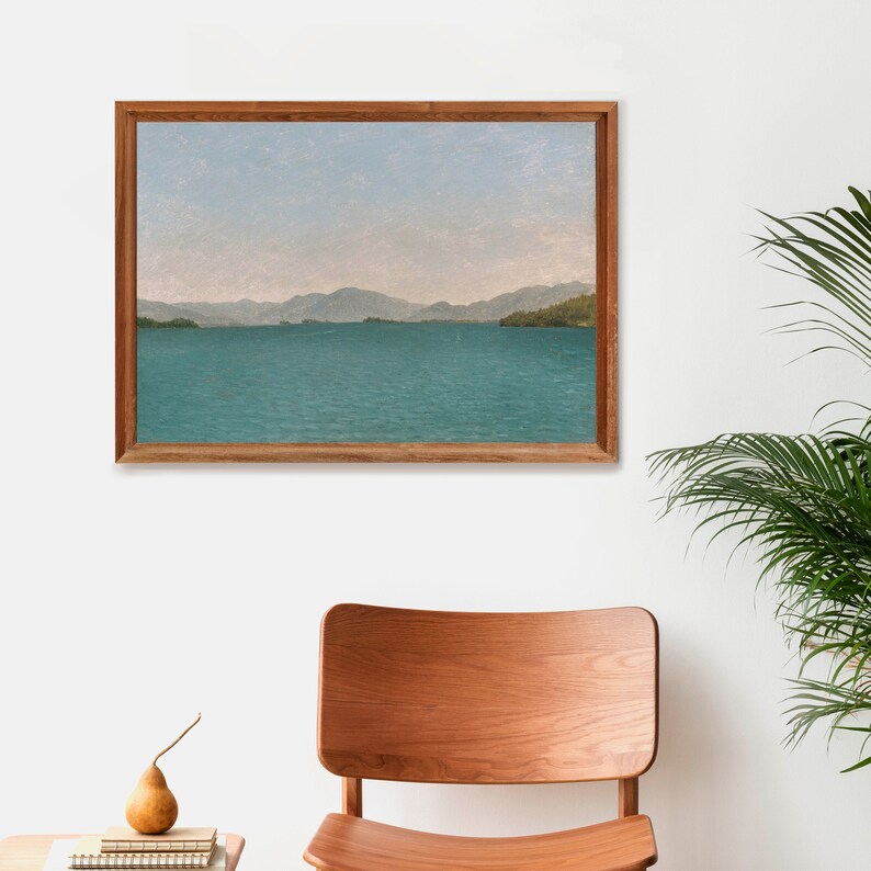 May include: A framed painting of a landscape with a body of water and mountains in the distance. The water is a light blue-green color and the mountains are a dark green color. The sky is a light blue color.