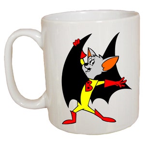 May include: White ceramic mug with a cartoon image of a gray bat superhero with yellow and red costume, black wings, and the letter "B" on the chest.