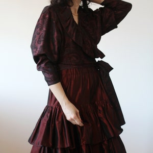 May include: A burgundy wrap top with a ruffled collar and long sleeves, paired with a burgundy skirt with multiple layers of ruffles.