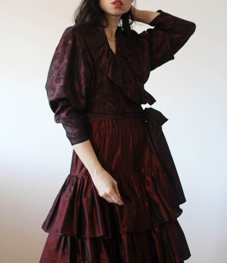 May include: A burgundy wrap top with a ruffled collar and long sleeves, paired with a burgundy skirt with multiple layers of ruffles.