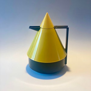 Könnte beinhalten: Eine gelbe und schwarze Teekanne aus Keramik mit einem konischen Deckel und einem Henkel.