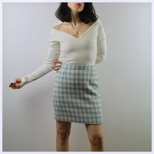 Op de afbeelding: Een wit, lang mouwig top met off-shoulder, gecombineerd met een blauwe en witte geruite minirok.