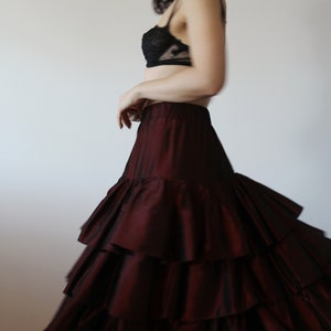 May include: A woman wearing a black lace bra and a burgundy ruffled skirt. The skirt has multiple layers of ruffles and is flowing.
