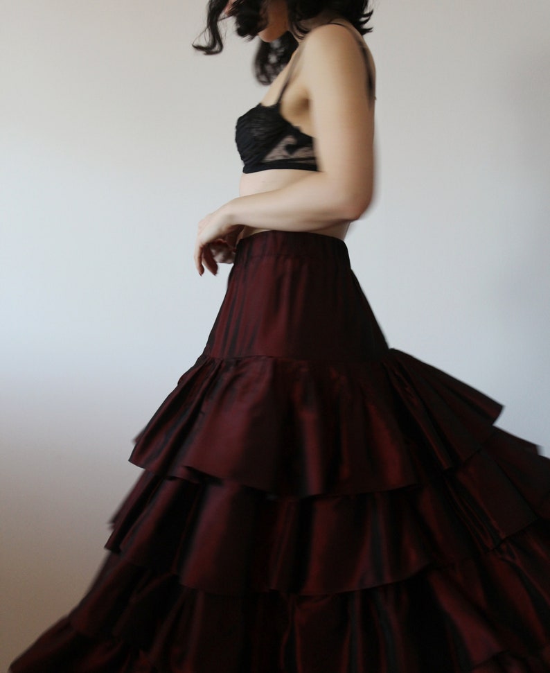 May include: A woman wearing a black lace bra and a burgundy ruffled skirt. The skirt has multiple layers of ruffles and is flowing.