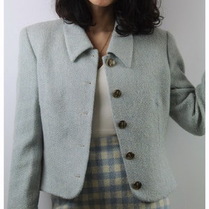 Op de afbeelding: Een lichtblauwe blazer met een herringbone-patroon en gouden knopen. De blazer heeft een getailleerde lengte en een kraag.