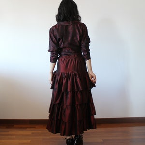 May include: A burgundy brocade blouse with long sleeves and a ruffled skirt. The skirt has multiple layers of ruffles and is a deep burgundy color.