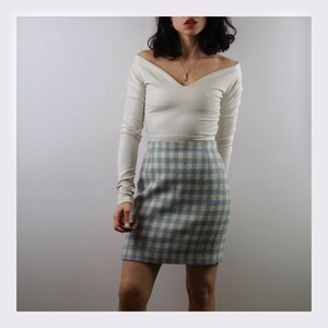 Op de afbeelding: Een wit off-shoulder longsleeve top gecombineerd met een blauw-wit geruite minirok.