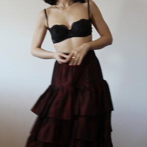 May include: A woman wearing a black lace bra and a burgundy tiered skirt.