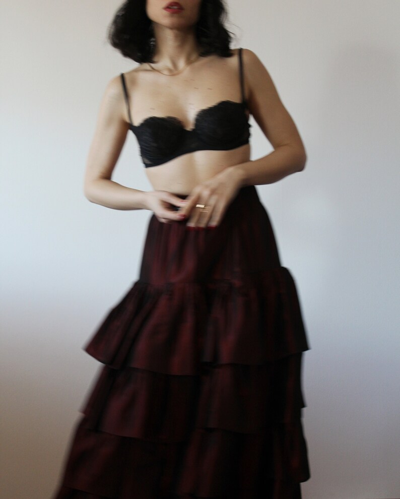 May include: A woman wearing a black lace bra and a burgundy tiered skirt.