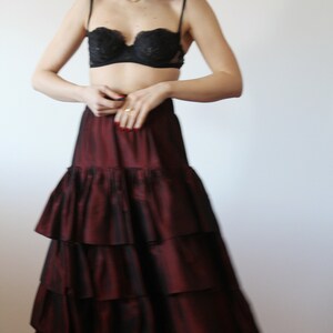 May include: A woman wearing a black lace bra and a long, burgundy, tiered skirt. The skirt has multiple layers of ruffles.