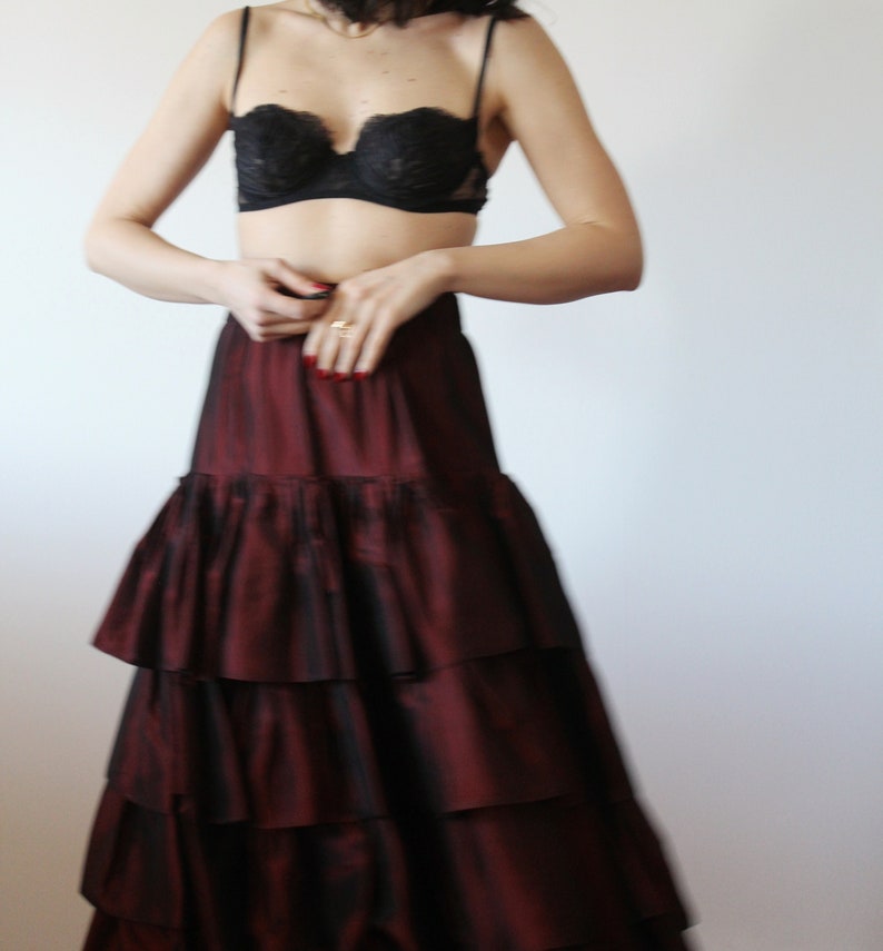 May include: A woman wearing a black lace bra and a long, burgundy, tiered skirt. The skirt has multiple layers of ruffles.