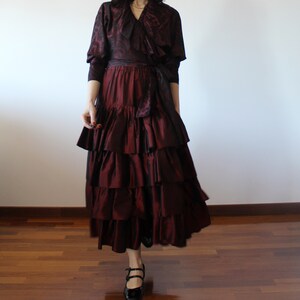 May include: A burgundy ruffled skirt with a matching burgundy patterned top. The top has a ruffled collar and a tie at the waist.