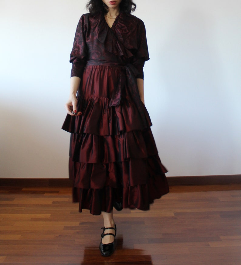 May include: A burgundy ruffled skirt with a matching burgundy patterned top. The top has a ruffled collar and a tie at the waist.