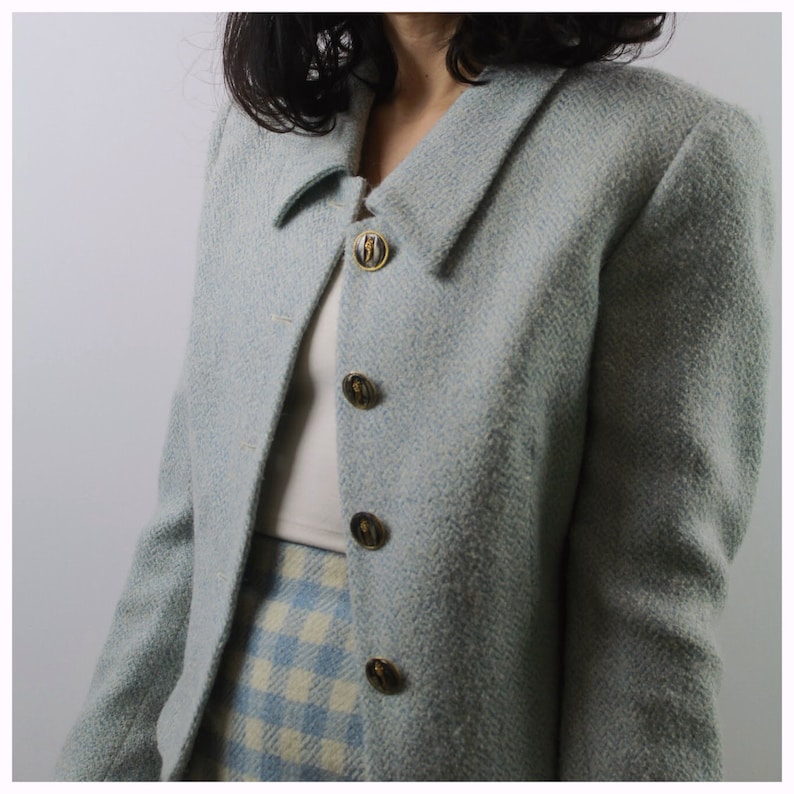 Op de afbeelding: Een lichtblauwe blazer met een wit en lichtblauw geruite rok. De blazer heeft gouden knopen met een zwart ontwerp.
