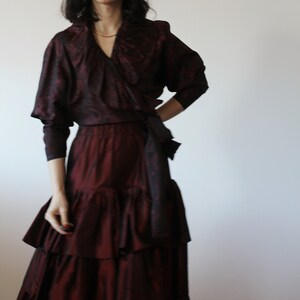 May include: A burgundy silk dress with a ruffled skirt and a wrap top. The top has a V-neckline and a long sleeve.