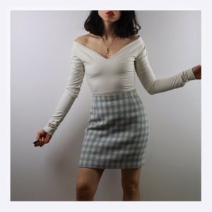 Op de afbeelding: Een wit longsleeve shirt met een v-hals en een blauw-wit geruite rok.