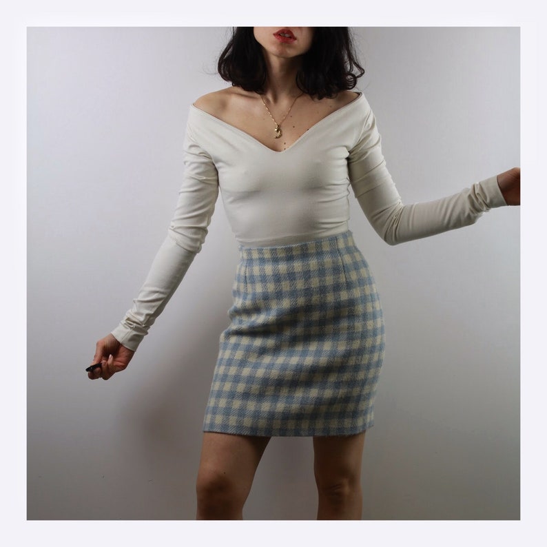 Op de afbeelding: Een wit longsleeve shirt met een v-hals en een blauw-wit geruite rok.