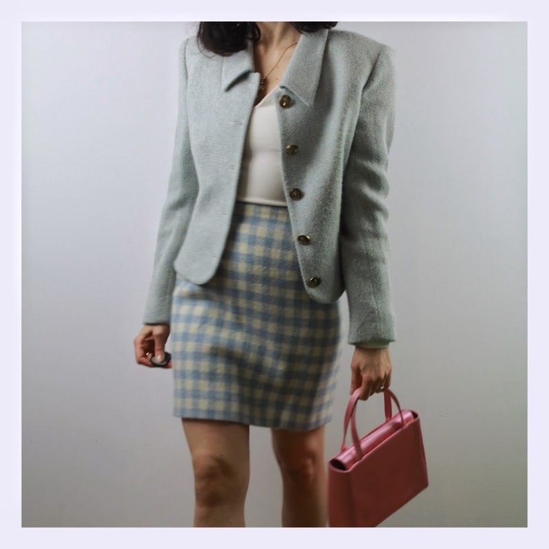 Op de afbeelding: Een lichtblauwe blazer met een wit en lichtblauw geruite rok en een roze handtas.