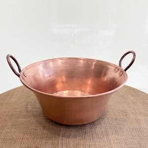 May include: A large copper bowl with two handles. The bowl has a hammered finish and is sitting on a burlap surface.