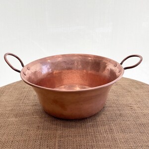 May include: A large, hammered copper bowl with two handles. The bowl is sitting on a burlap surface.