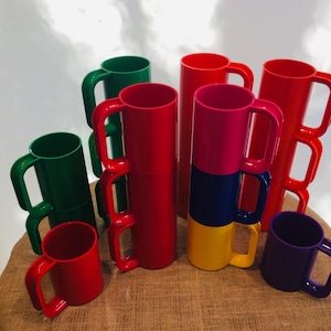 May include: A set of colorful plastic mugs with double handles. The mugs are red, green, purple, and yellow.
