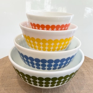 May include: Set of four nesting mixing bowls with a retro design. The bowls are white with a band of colorful polka dots in orange, yellow, blue, and green.